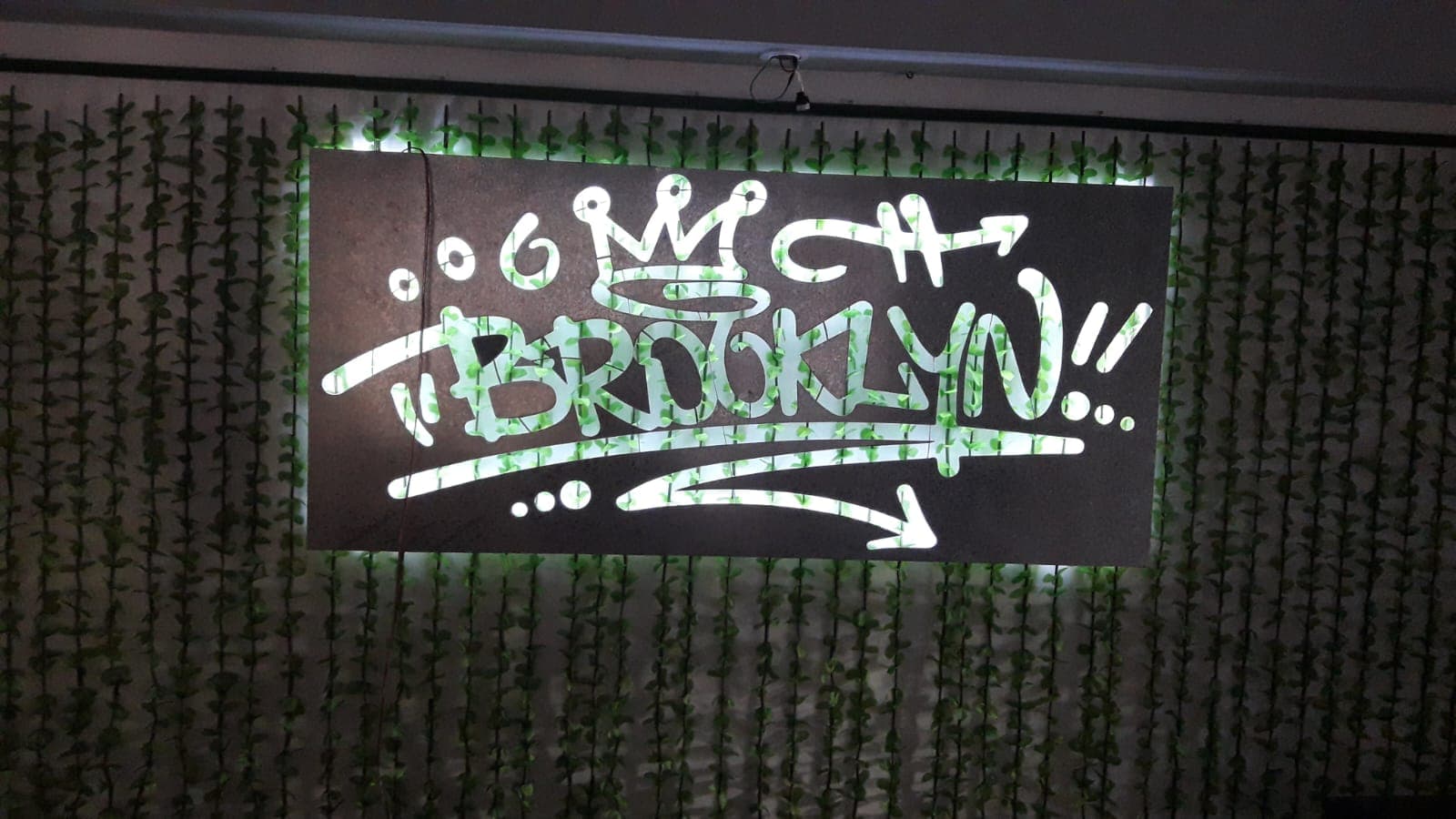 Cartel de chapa con letras caladas e iluminación LED montado sobre una pared verde