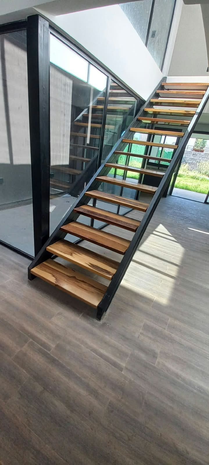 Escalera metálica con peldaños de madera y viga central negra en una casa moderna