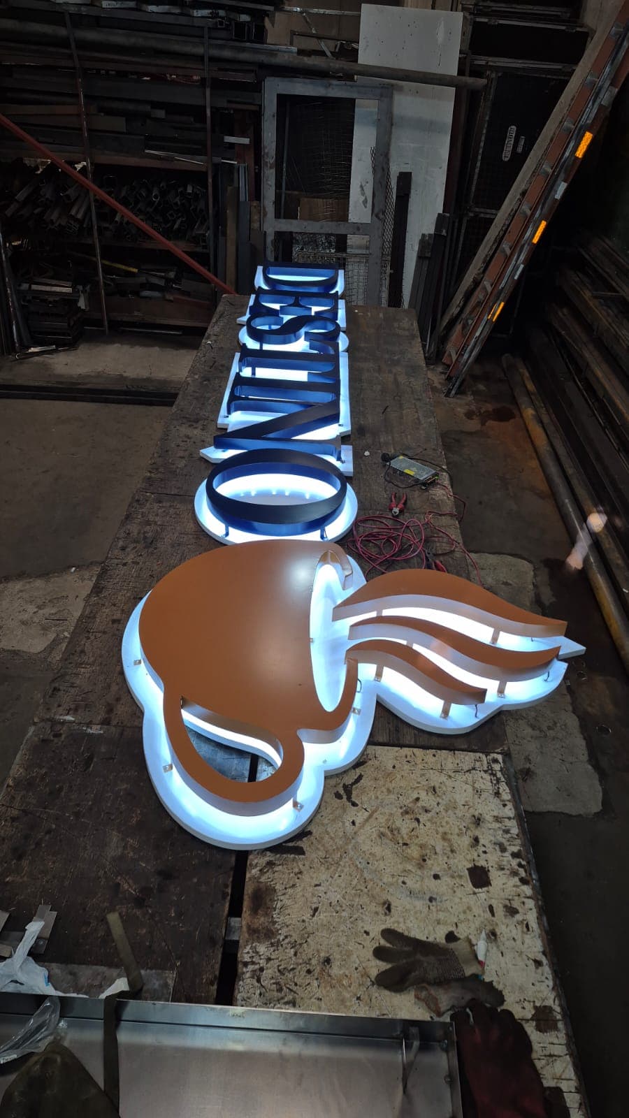 Letras corpóreas y un isologo con iluminación LED encendida sobre la mesa del taller