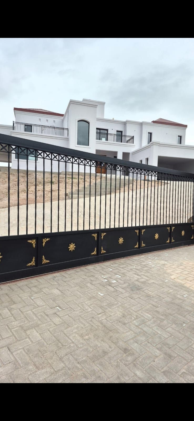 Portón corredizo negro con apliques dorados instalado en el acceso de una vivienda