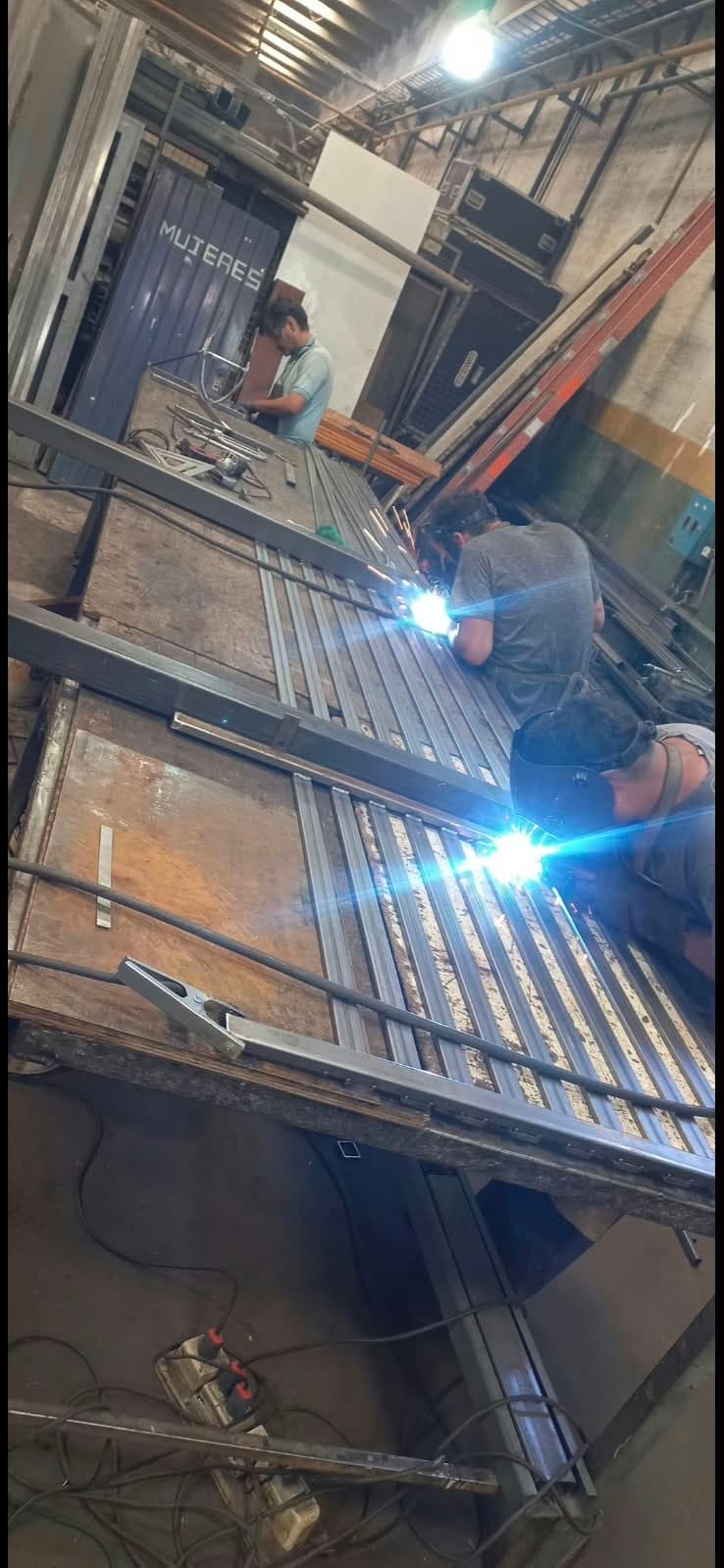 Dos operarios soldando una estructura metálica sobre la mesa de trabajo del taller